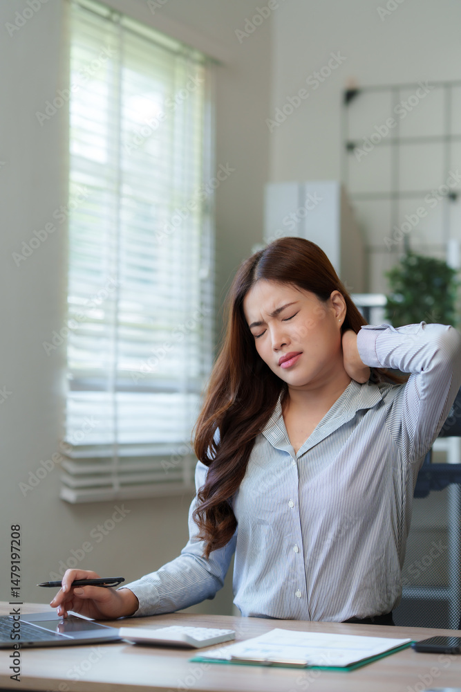 Asian businesswoman suffering from neck pain while working on laptop in office Asian businesswoman suffering from neck pain while working on laptop in office