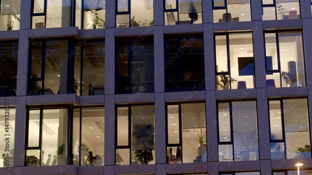 Office building facade with illuminated windows at dusk, showcasing workspaces and design. Office building facade with illuminated windows at dusk, showcasing workspaces and design.