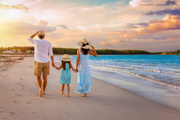 A beautiful family on summer holidays walks on a tropical beach during golden sunset time as a concept for travel and vacations