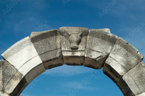 Ancient stone arch and keystone with bull head on entrance to the amphitheatre in blue sky