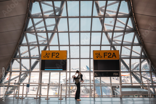 Happy mother holding and lifting her little girl daughter in the air before departure for travel in front of airport gate 