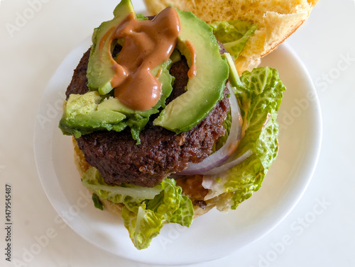 Burger with beef patty on lettuce topped with avocado slice and burger sauce served on green marble chopping board 