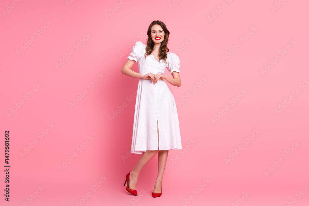 Elegant young woman in white dress making heart sign with hands against a pink background Elegant young woman in white dress making heart sign with hands against a pink background