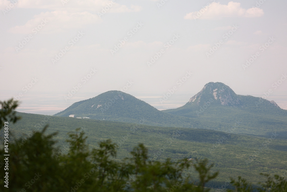 Obraz premium Scenic View Of Mount Beshtau And Mount Zheleznaya From The Slopes Of Mount Mashuk, Pyatigorsk, Russia. Forested Hills Under A Hazy Summer Sky. Caucasus Mountains.