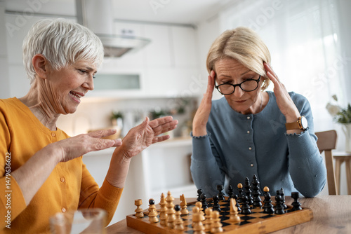 Senior women playing chess, having fun and enjoying retirement at home