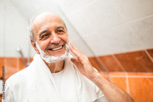 Wallpaper Mural Happy senior man with wrinkled skin applying foam on his face and preparing for shaving while standing in front of bathroom mirror. Torontodigital.ca