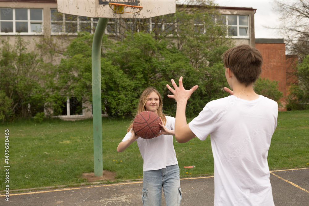 Obraz premium Two energetic teens are playing basketball together outside on a vibrant playground court, enjoying the friendly competition