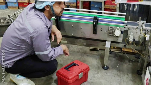 Male technician engineering department with tool box inspects the operation machinery and conveyor belt during transport canned fish into boxes in the packing room of canned fish factory.