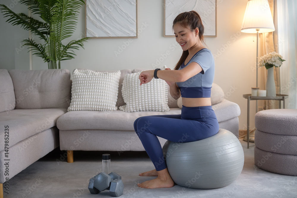Obraz premium Woman checking her smartwatch while sitting on an exercise ball during a home workout.