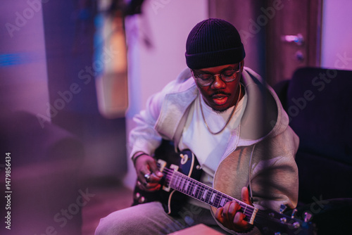 A diverse musician passionately plays an electric guitar in a cozy music studio, creating an artistic atmosphere. The ambient lighting highlights the creative process and musical expression.