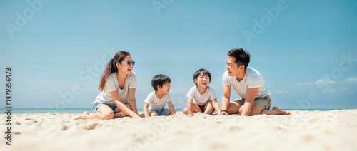Young asian family sitting on a beach on a clear blue sky day playing with two children and laughing