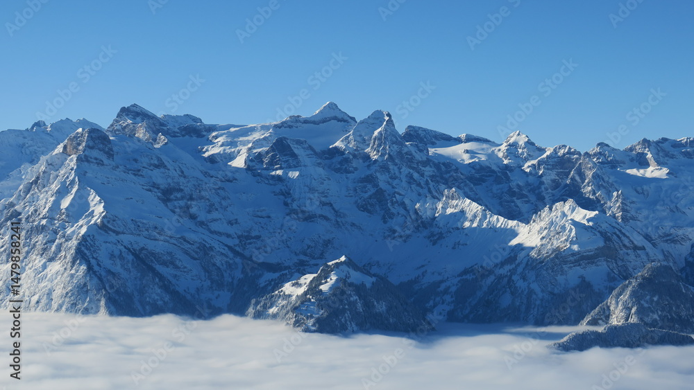 Fototapeta premium Stunning panoramic view of snow-capped peaks and clouds. Perfect for winter, nature, and travel themes.