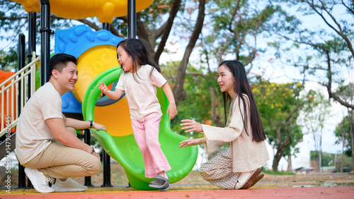 Happy child finishing a slide with supportive parents waiting and smiling at the bottom.