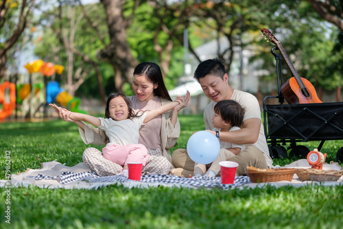 Joyful family enjoying picnic time at the park with kids playing and parents relaxing together.