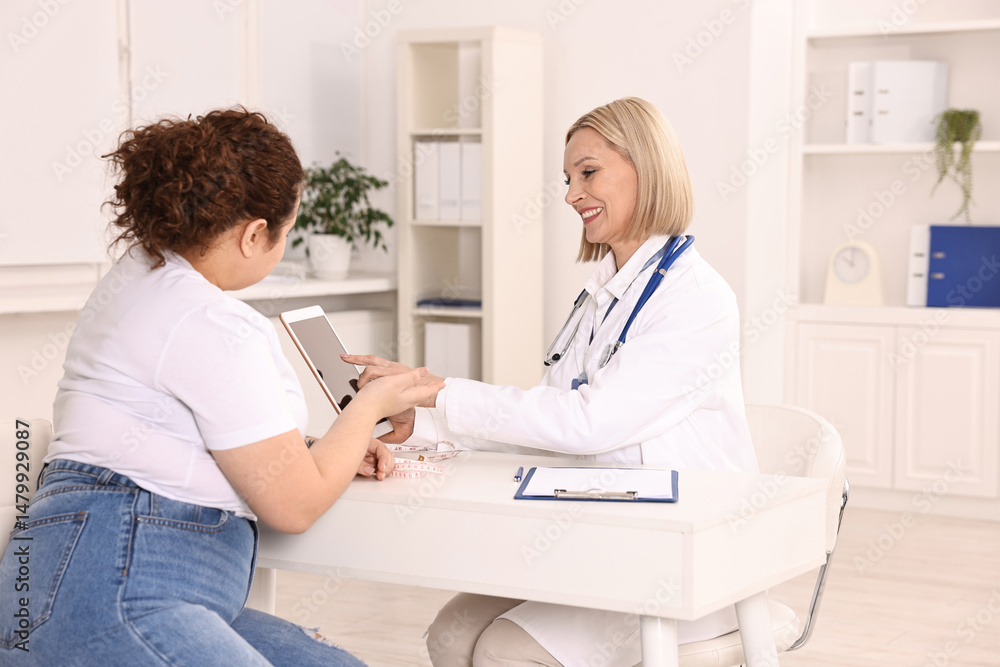Weight loss. Smiling nutritionist with tablet consulting patient at table in clinic Weight loss. Smiling nutritionist with tablet consulting patient at table in clinic