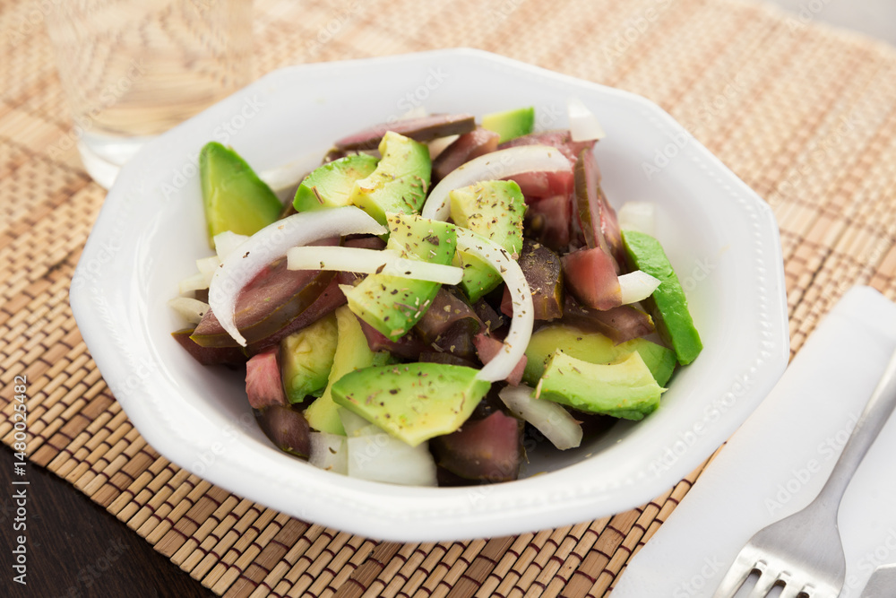 Salad of black tomatoes, avocado and onions in white ceramic bowl