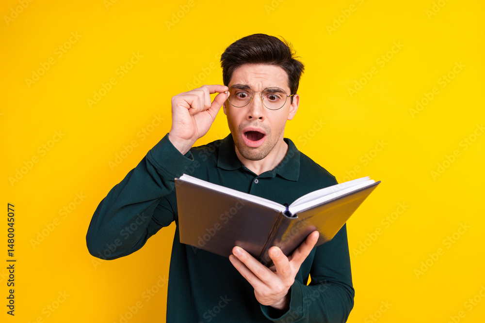 Surprised Young Man Reading a Book Standing Against a Vibrant Yellow Background, Wearing Green Casual Polo Shirt and Glasses Surprised Young Man Reading a Book Standing Against a Vibrant Yellow Background, Wearing Green Casual Polo Shirt and Glasses