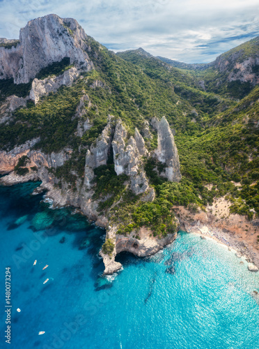 Fototapeta Naklejka Na Ścianę i Meble -  Aerial view of rocks and mountains, blue bay, beach, boats on sunny summer day. Cala Goloritze, Sardinia Island, Italy. Top drone view of cliffs, stones, green trees, transparent azure water at sunset