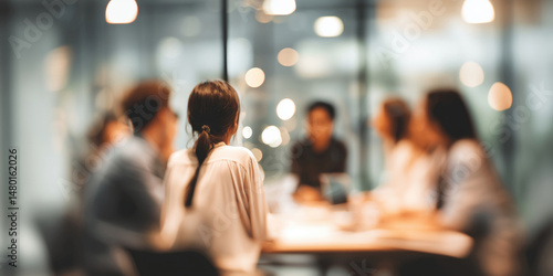 Group of people in a blurred meeting room, focused on back of a woman's head
