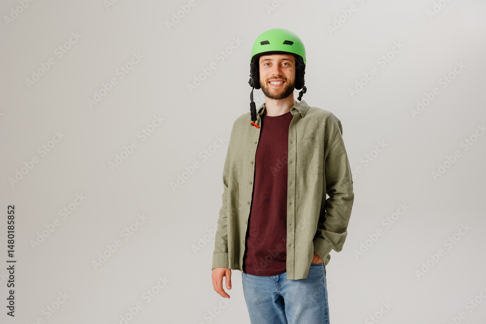Fototapeta premium Young man dressed casually with a green helmet poses confidently in a studio setting while smiling