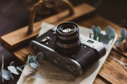 Retro camera on old book and eucalyptus branch on wooden background, flat lay. Vintage style