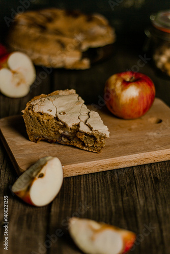 Traditional apple pie Charlotte apples are lying nearby. Sweet Thanksgiving dinner, autumn seasonal apple pie sliced one piece on wooden tray, on dark wooden background.