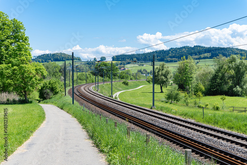 A winding railway line through a green landscape on a sunny day, surrounded by trees and hills.