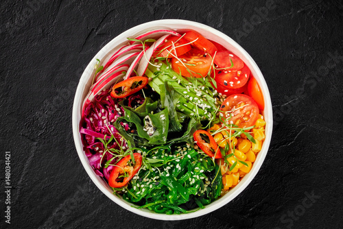 Poke bowl with wakame seaweed, tomatoes, corn and radish on dark background