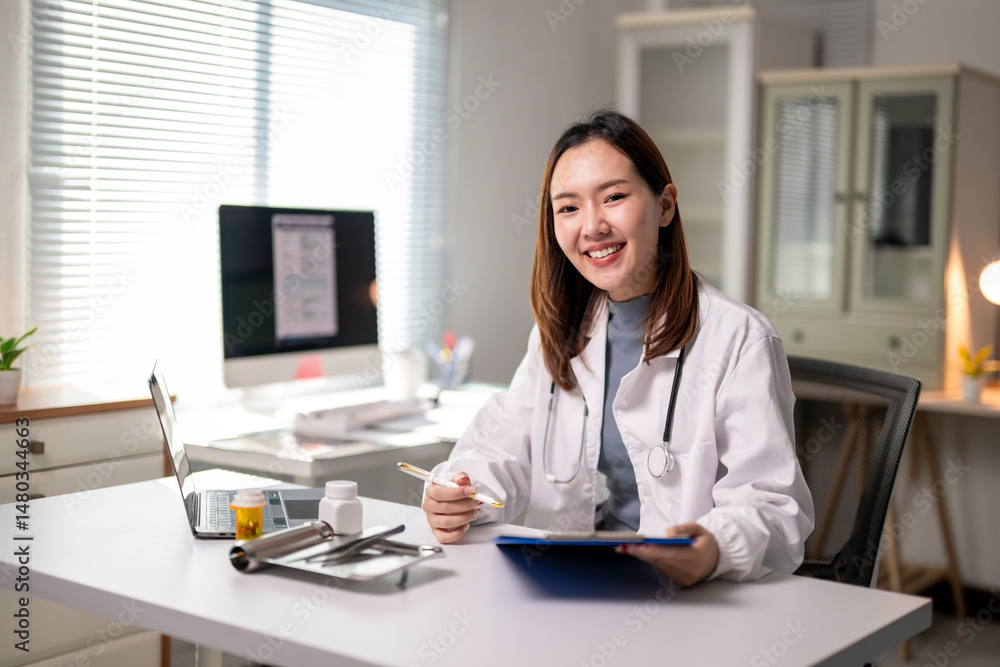 A woman in a white lab coat is sitting at a desk with a clipboard and a laptop A woman in a white lab coat is sitting at a desk with a clipboard and a laptop