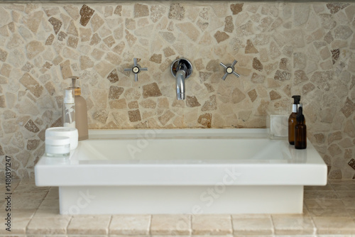 White sink basin is sitting on stone countertop, displaying chrome faucet and cosmetic bottles