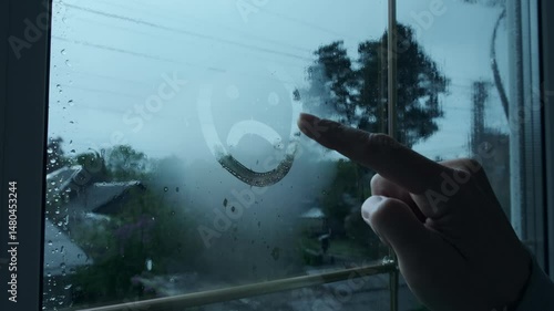 Depressed Mood Concept. Finger Draws Sad Face on Steamy Window While It Rains Outside. Drawing Sad Emotion on Glass. Mood of Isolation and Melancholy. Seasonal depression