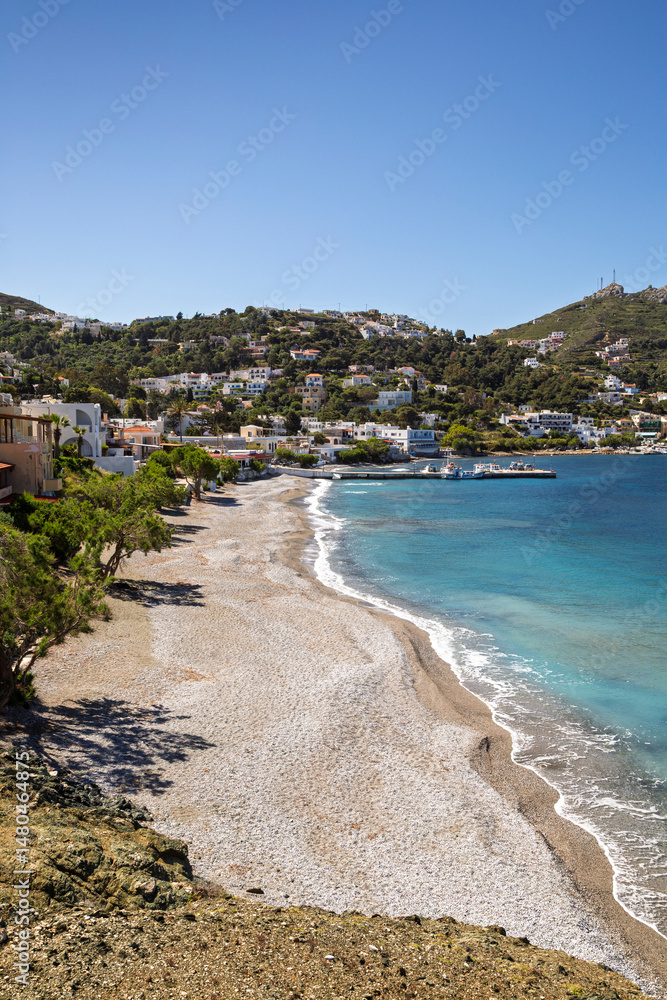 Scenic view of a beach and buildings along the hilly coast in the idyllic village of Myrties (Mirties) on Kalymnos island in Greece on a sunny day. Scenic view of a beach and buildings along the hilly coast in the idyllic village of Myrties (Mirties) on Kalymnos island in Greece on a sunny day.
