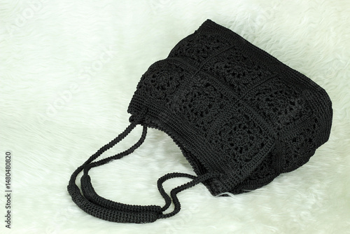 Black bag crochet with square motif and rectangular base isolated on white furry blanket.