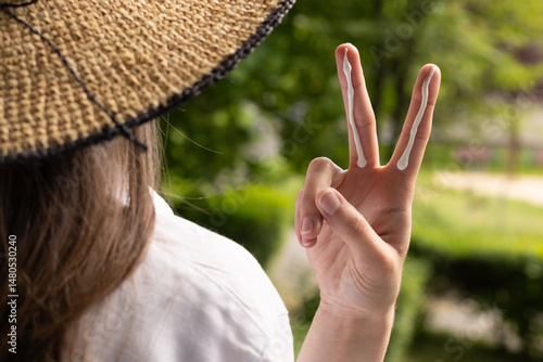 Canvas Print Closeup of a woman in a hat applying sufficient amount of sunscreen for the face and neck – two finger lengths