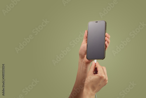 female hand plugging charger cord into smartphone to charge battery on green background, Wired charging