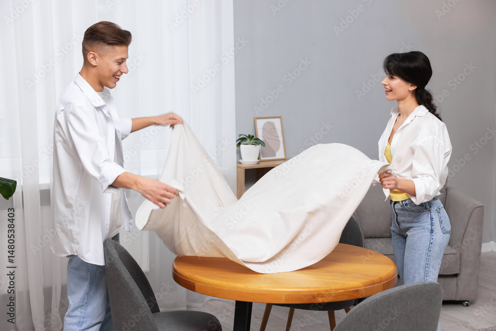 Obraz premium Couple putting white tablecloth on table at home