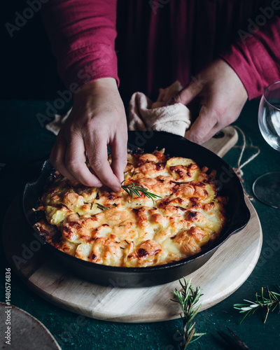 Chef preparing cheesy potato dish with rosemary garnish