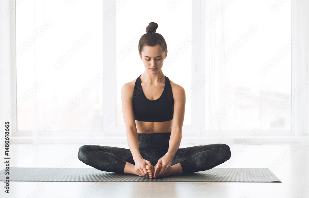 Fototapeta premium Pilates. Calm girl working out doing yoga exercise, sitting in baddha konasana, bound angle or butterfly pose, copyspace