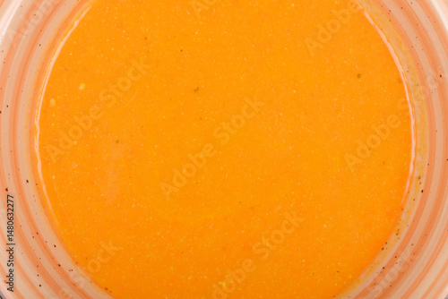 A top-down close-up shows a smooth, vibrant orange carrot soup in a bowl with light orange stripes