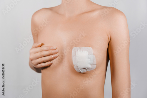 Patient covering breast with hand after tumor removal surgery, showing large adhesive bandage on clean skin in a close-up medical concept image