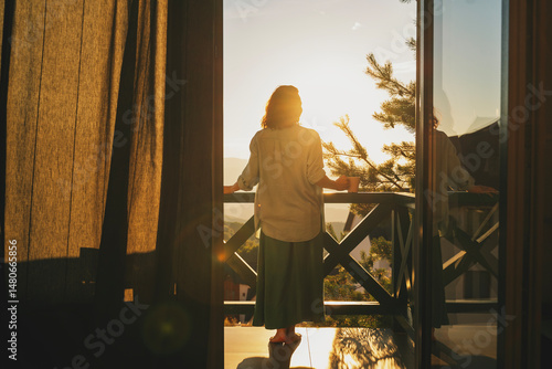 Fotografie Young woman standing on balcony and admiring view of sunset or sunrise in mounta