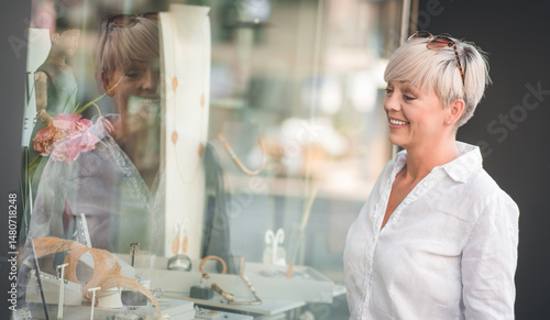 Happy woman looking at showcase or shop window chooses jewelry in store. Shopping time. Outdoors - outside