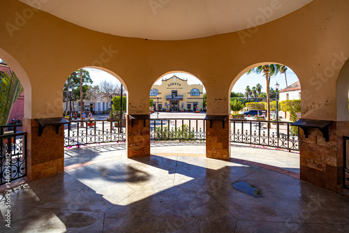 Main square and government palace seen from the inside of a kiosk, pillars, arches, metal railing, wall and yellow roof, sunny day in Loreto, Baja California Sur, Mexico