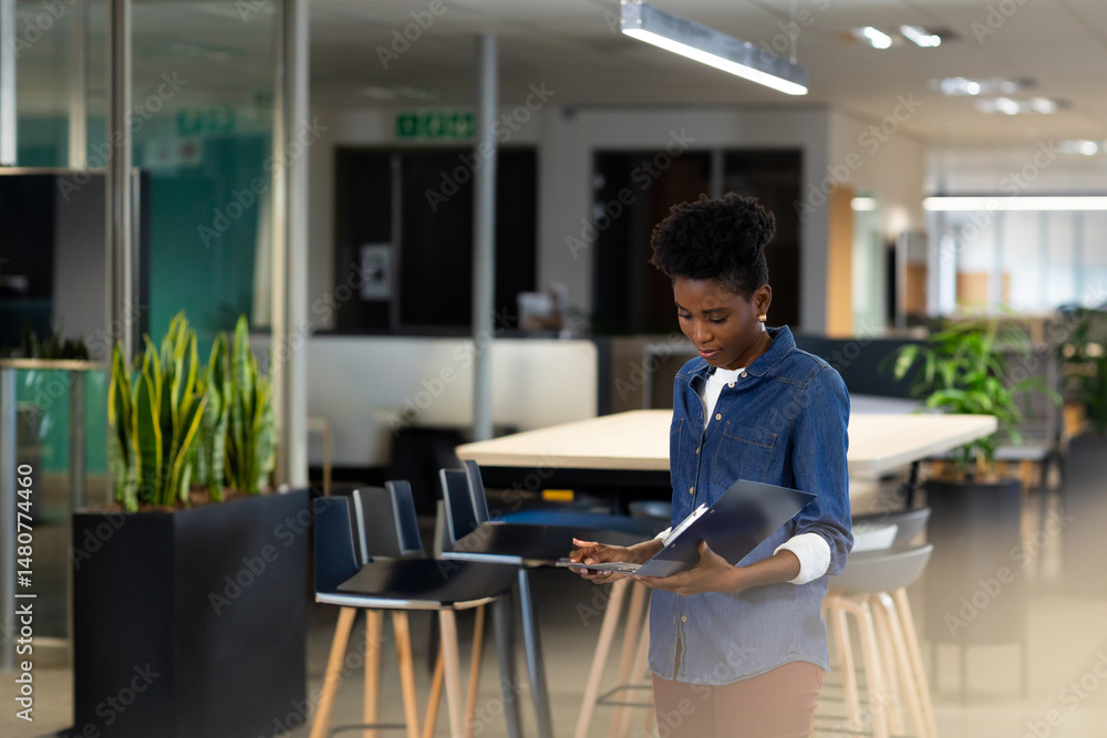African American woman examining documents at table in modern office, holding folder, copy space African American woman examining documents at table in modern office, holding folder, copy space