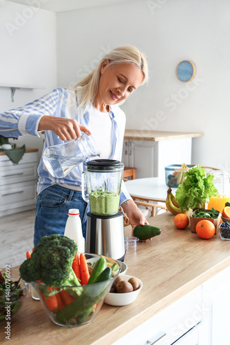 Mature woman making healthy smoothie with blender in kitchen