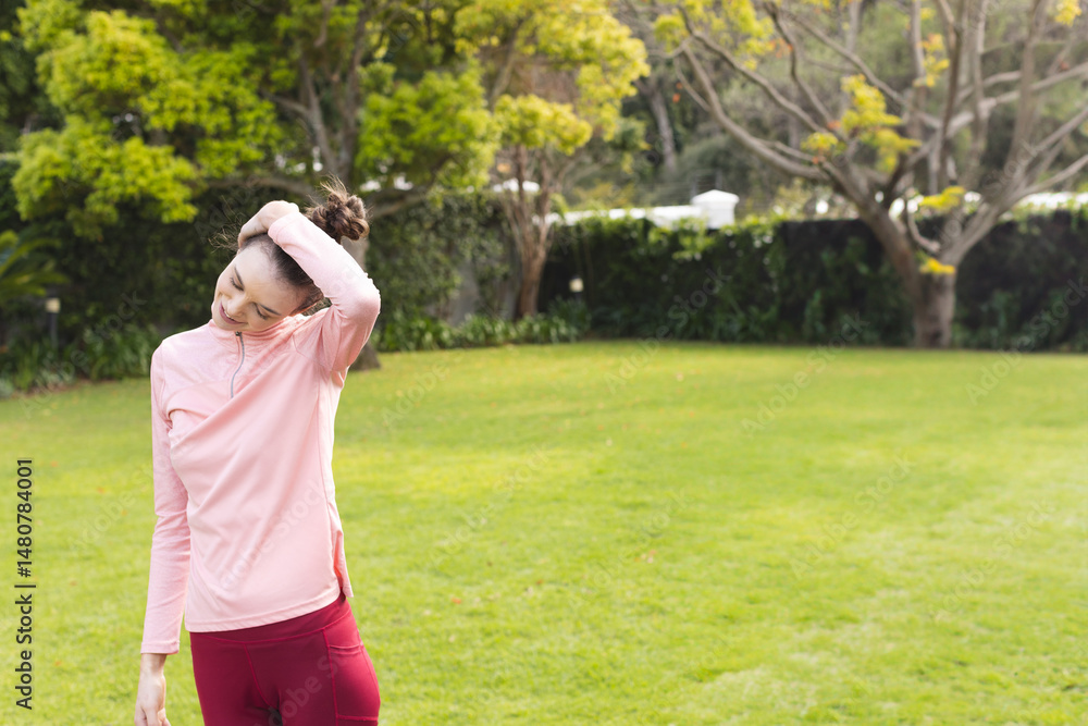 woman stretching neck on grassy lawn in garden, with pink top and burgundy leggings, copy space woman stretching neck on grassy lawn in garden, with pink top and burgundy leggings, copy space