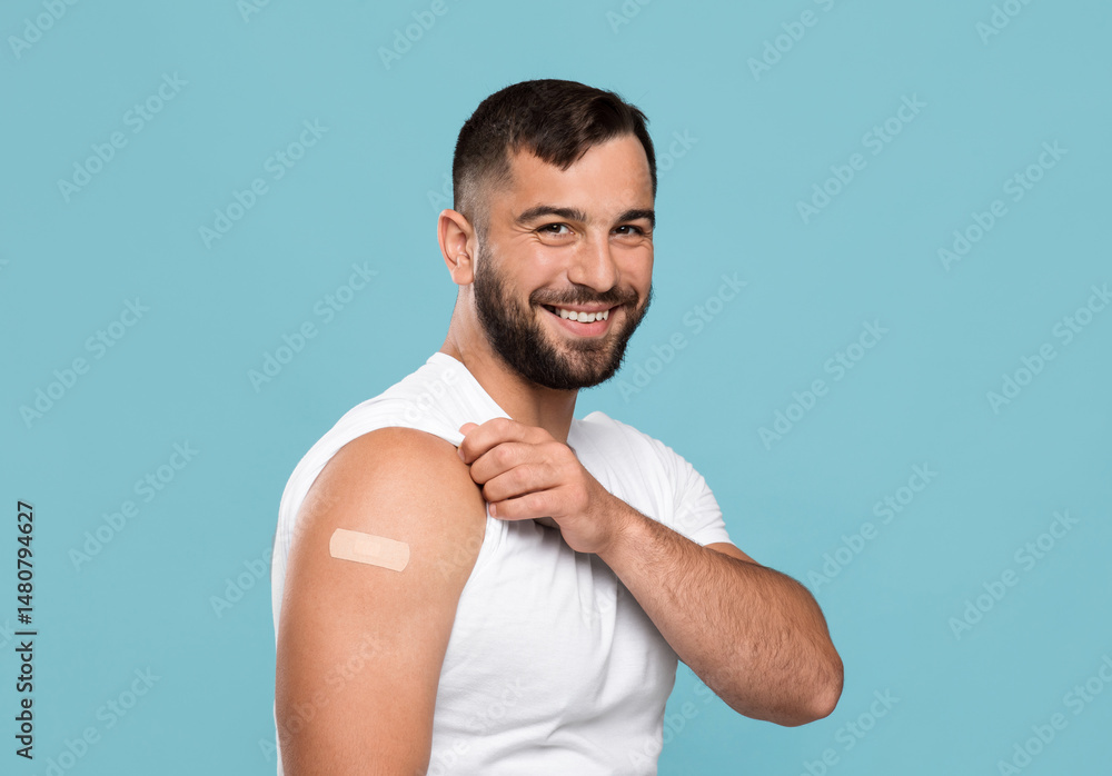 Smiling adult attractive caucasian guy show shoulder with band aid after vaccination, isolated on blue background. Health care, vaccine against flu and covid-19 virus, immunization of population Smiling adult attractive caucasian guy show shoulder with band aid after vaccination, isolated on blue background. Health care, vaccine against flu and covid-19 virus, immunization of population