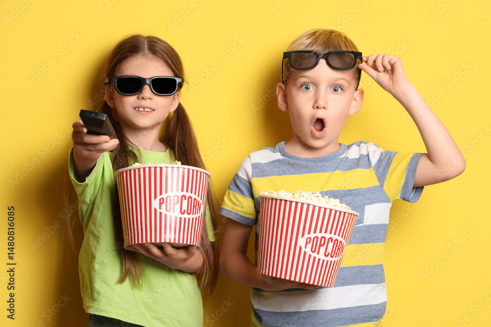 Fototapeta premium Little children in 3D glasses with popcorn watching TV on yellow background