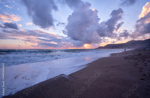 A tranquil coastal scene showcasing a sandy beach, vibrant sunset colors, waves, and dramatic clouds in a peaceful and calming natural ambiance..