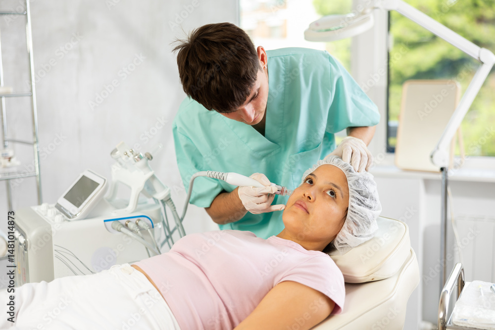 Obraz premium Young cosmetic doctor confidently utilizes hydrogen oxygen cleaning attachment on machine, providing client with impeccable skincare.